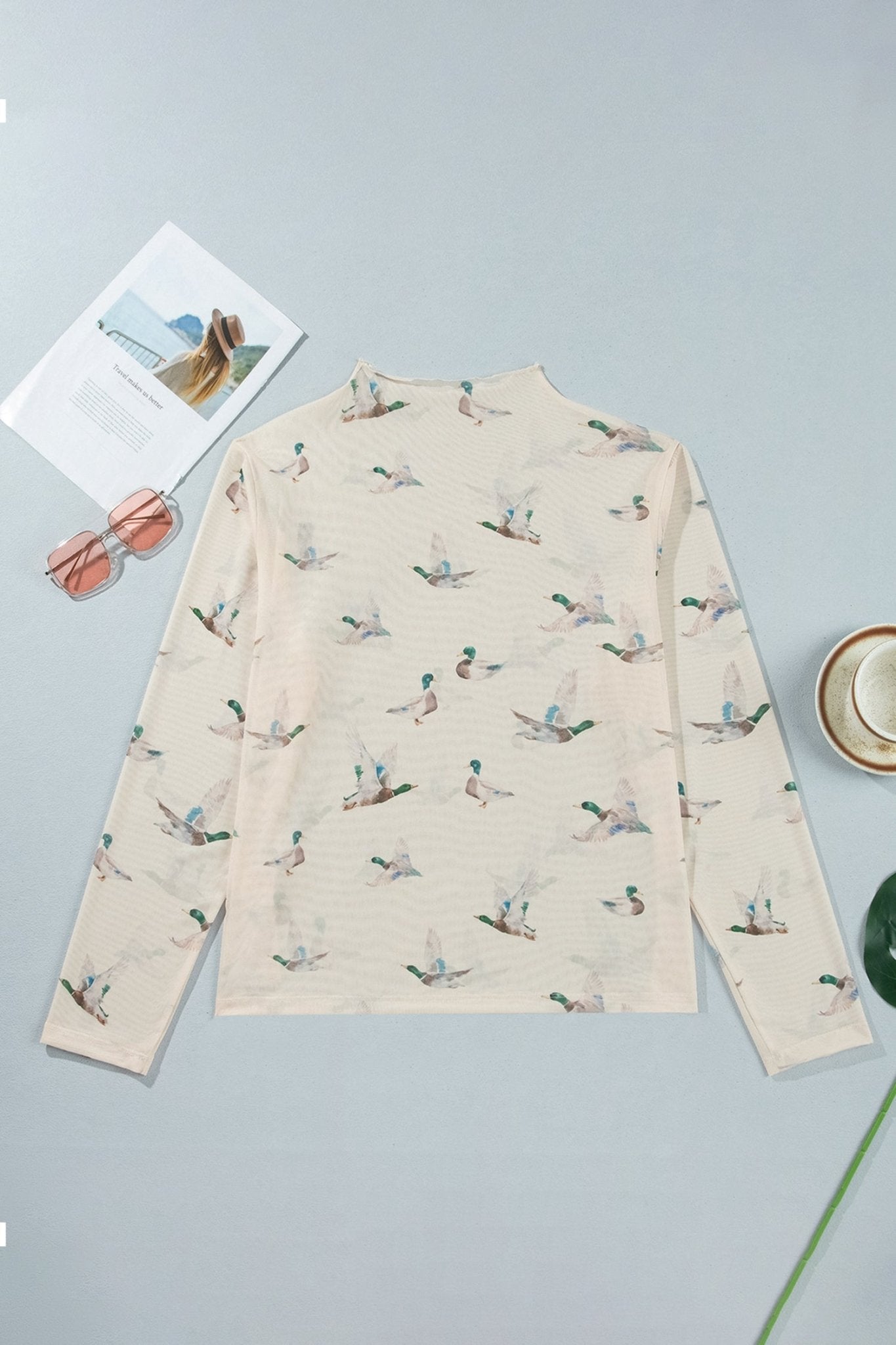 Cream mock-neck top with scattered duck print, sunglasses, and magazine.