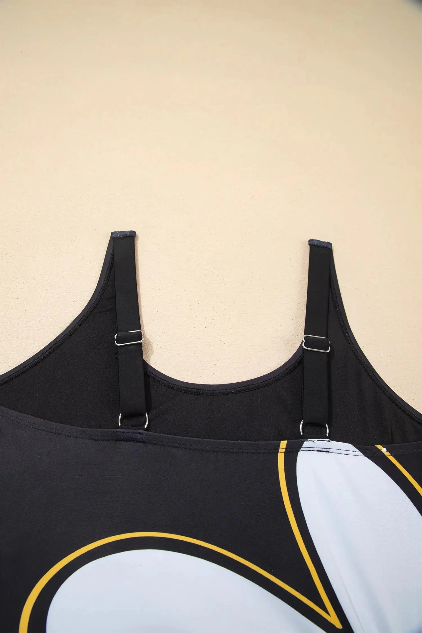 Close-up of black athletic tank top back straps and upper back against plain beige.