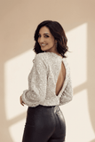 Woman wearing a sparkly silver top with a back cutout against a beige wall.