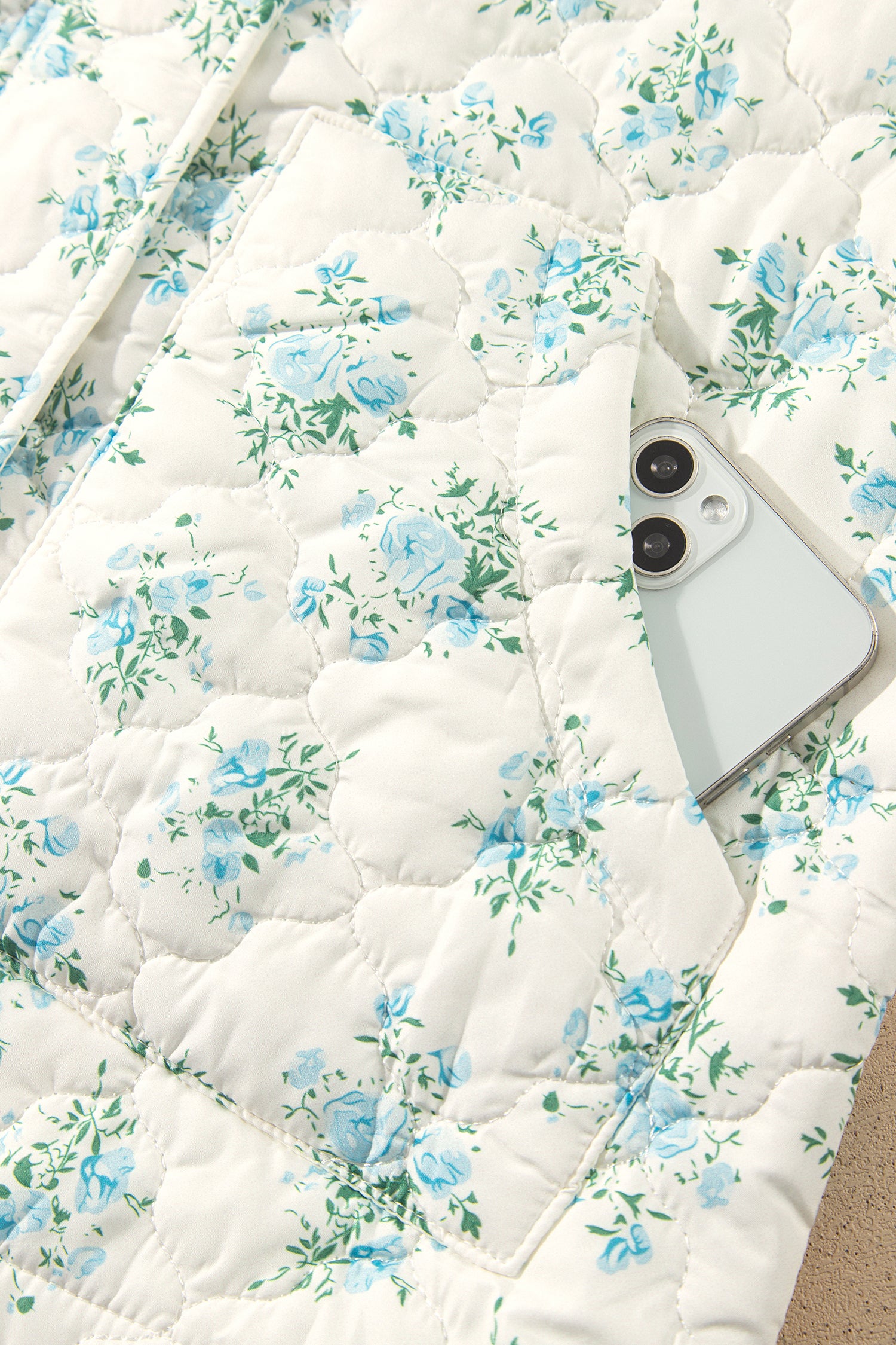 Close-up of front pocket holding a phone on sky blue floral quilted puffer jacket