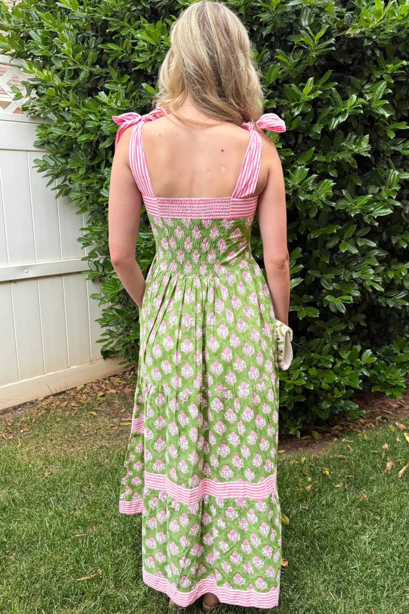 Woman wearing a green and pink dress with floral pattern standing in front of a bush.