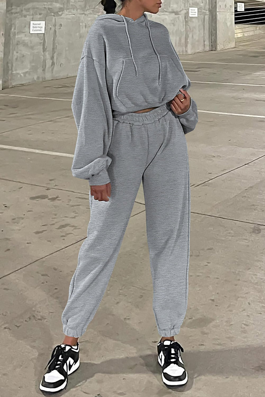 Person wearing a gray tracksuit with black and white sneakers on a concrete surface.