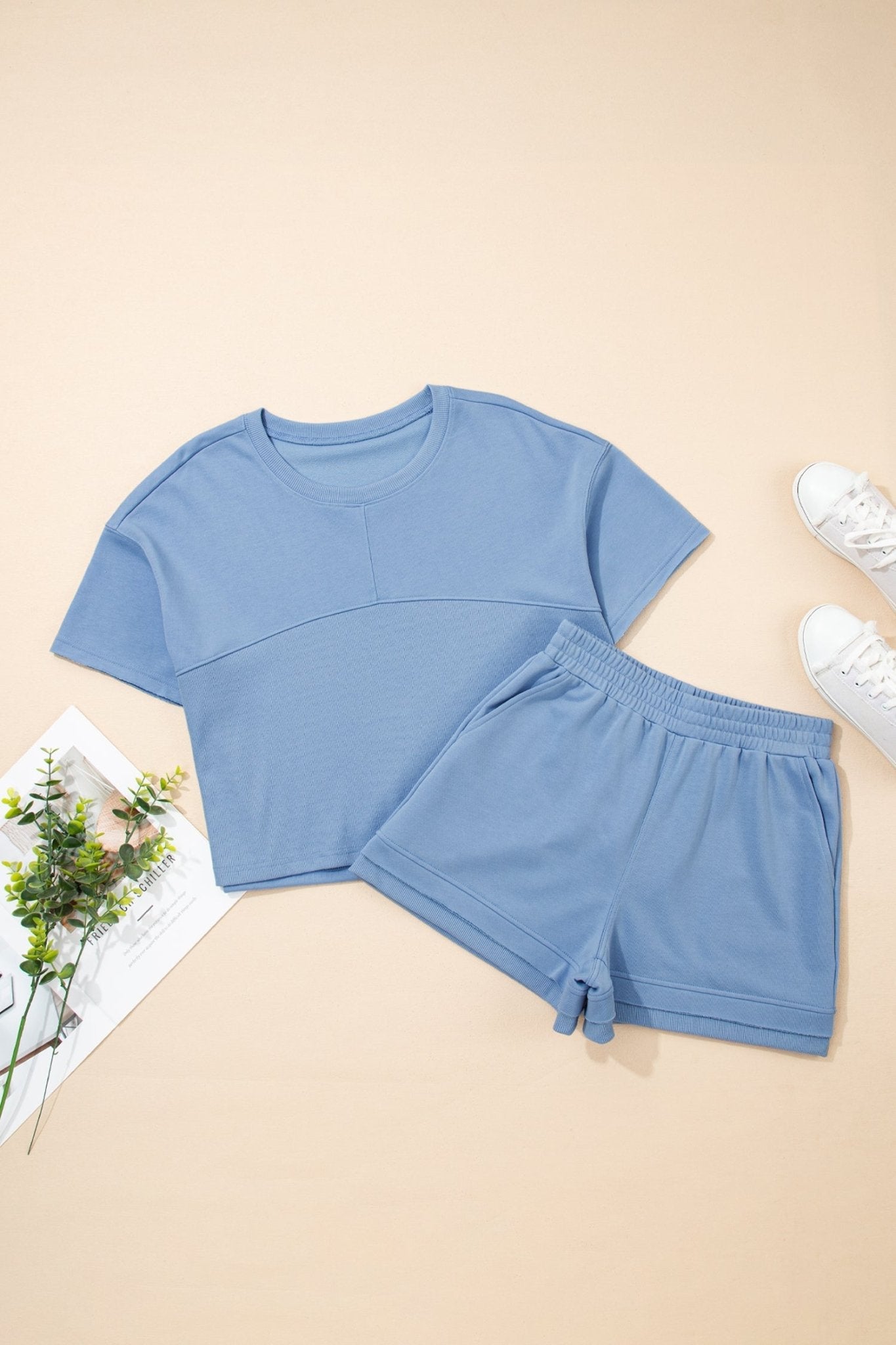 Blue crop top and shorts set on a beige surface with white sneakers and a plant.