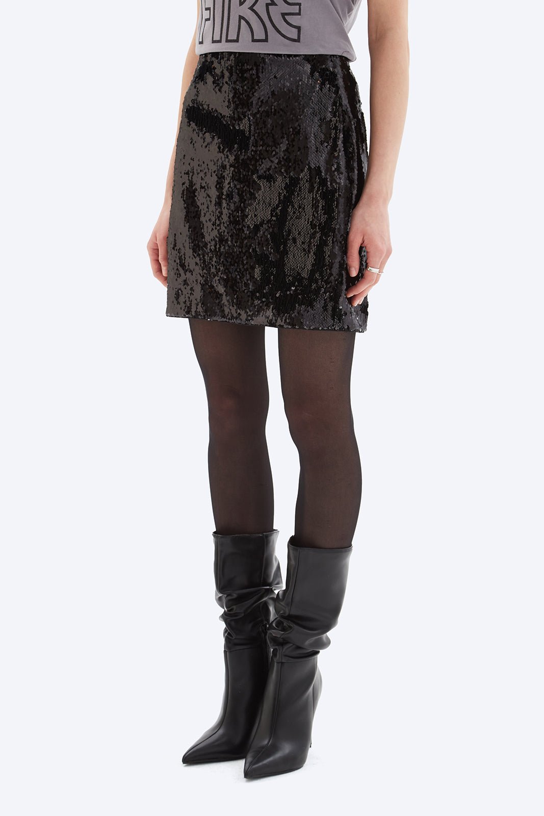 Person wearing a black sequin skirt and black knee-high boots on a white background