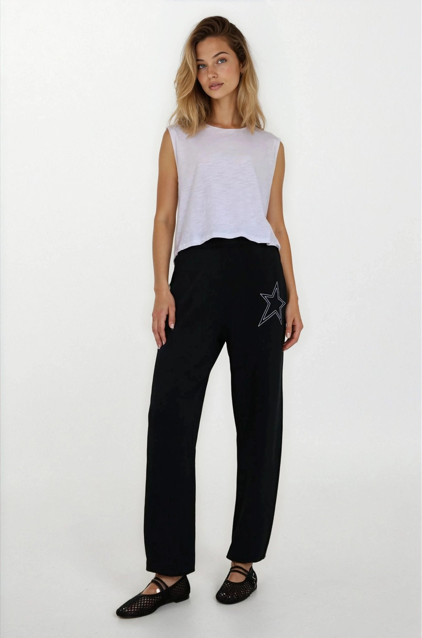 Woman wearing a white sleeveless top and black pants with a star design on a white background