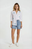 Woman wearing a white shirt with blue star patterns and denim shorts on a white background