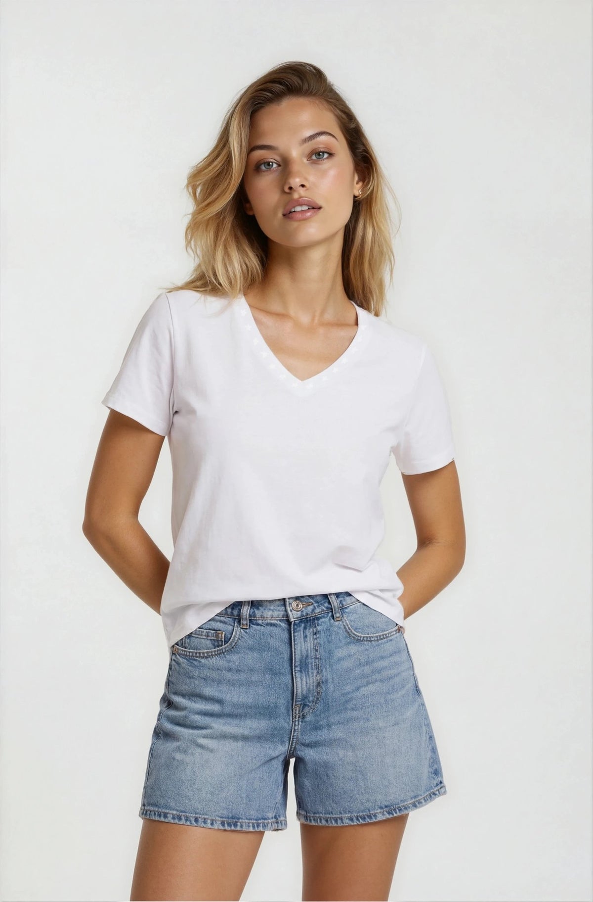 Woman wearing a white t-shirt and denim shorts on a plain background