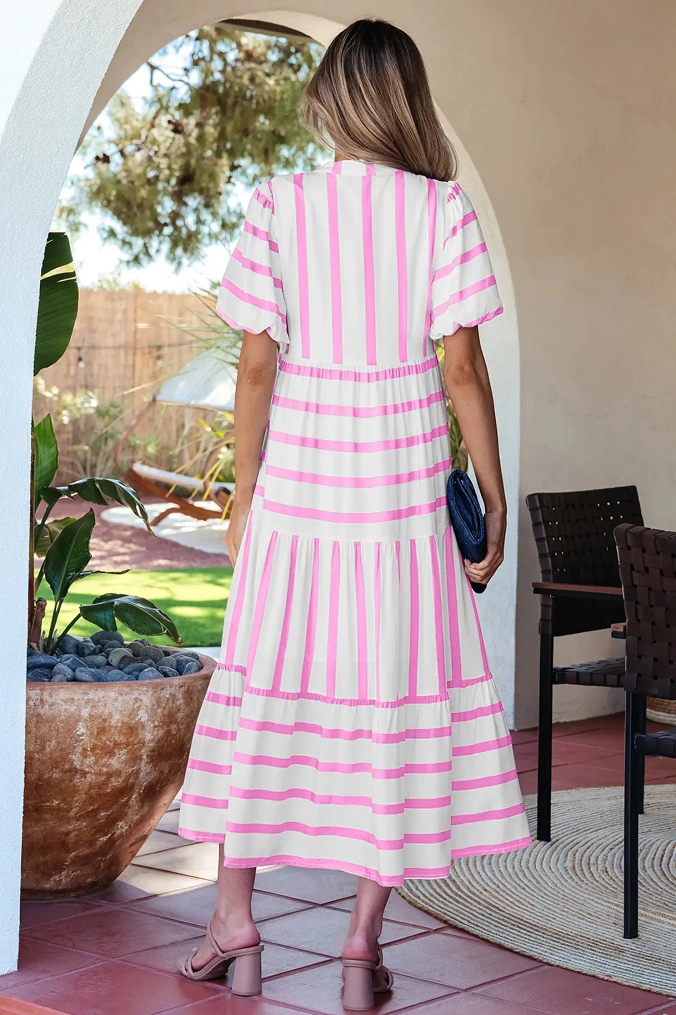 Woman in a pink and white striped dress standing in a sunlit outdoor area.