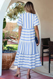 Woman in a blue and white striped dress standing by a poolside with a chair and table in the background.