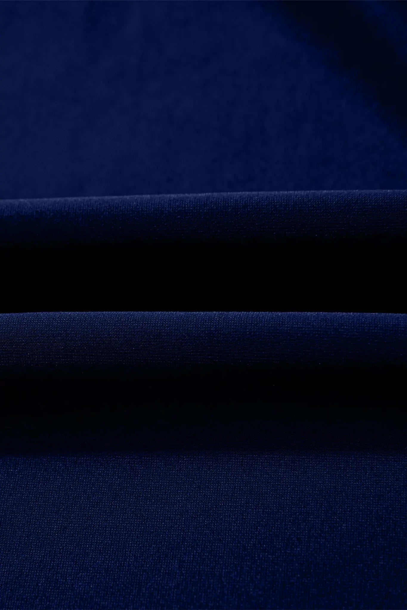 A close-up of dark navy blue fabric with soft horizontal folds showing the texture and color.