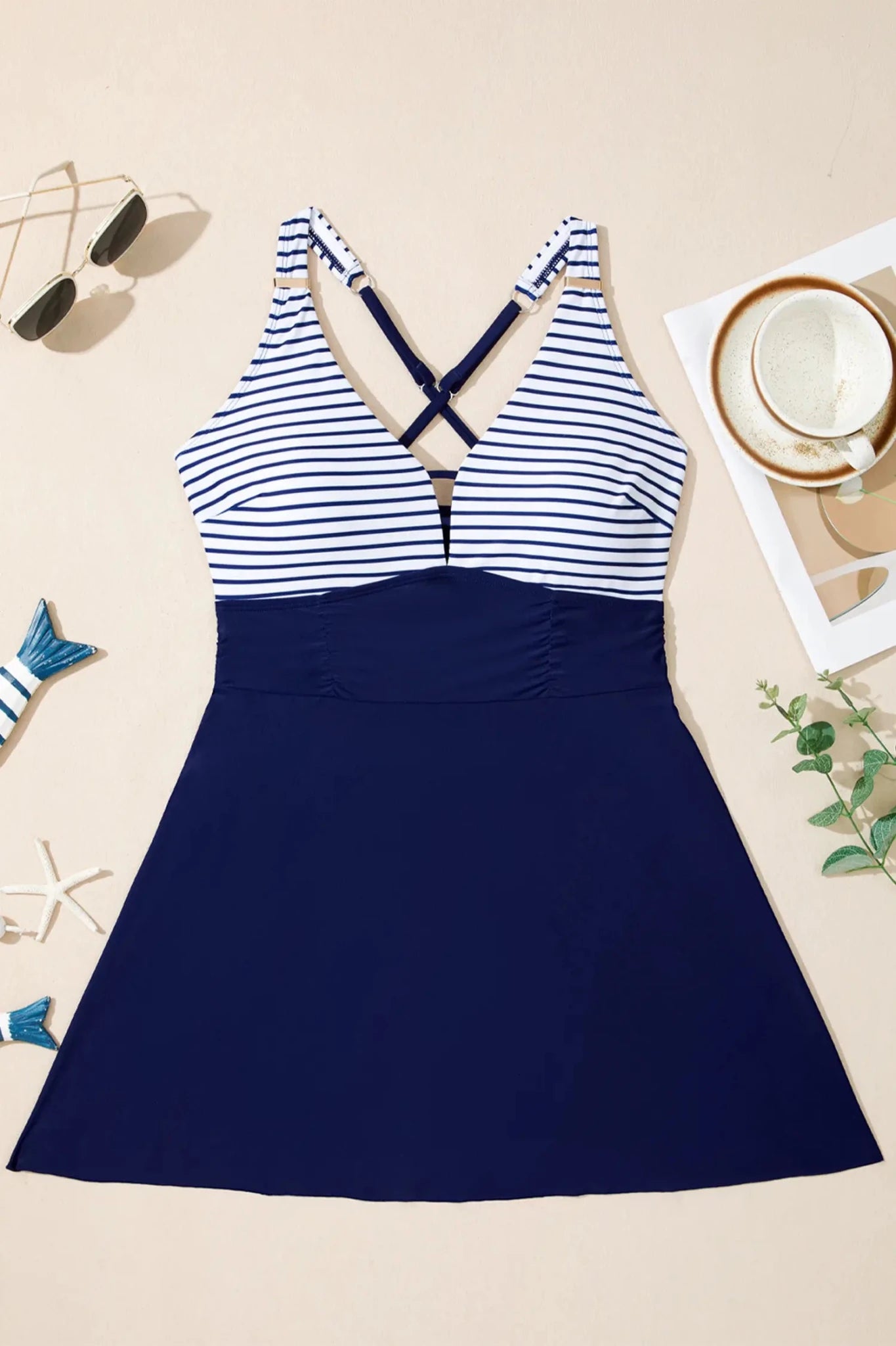 Navy and white striped swimsuit on a beige surface with sunglasses and a cup.
