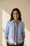 Woman wearing a blue striped shirt with leopard print trim against a beige wall.