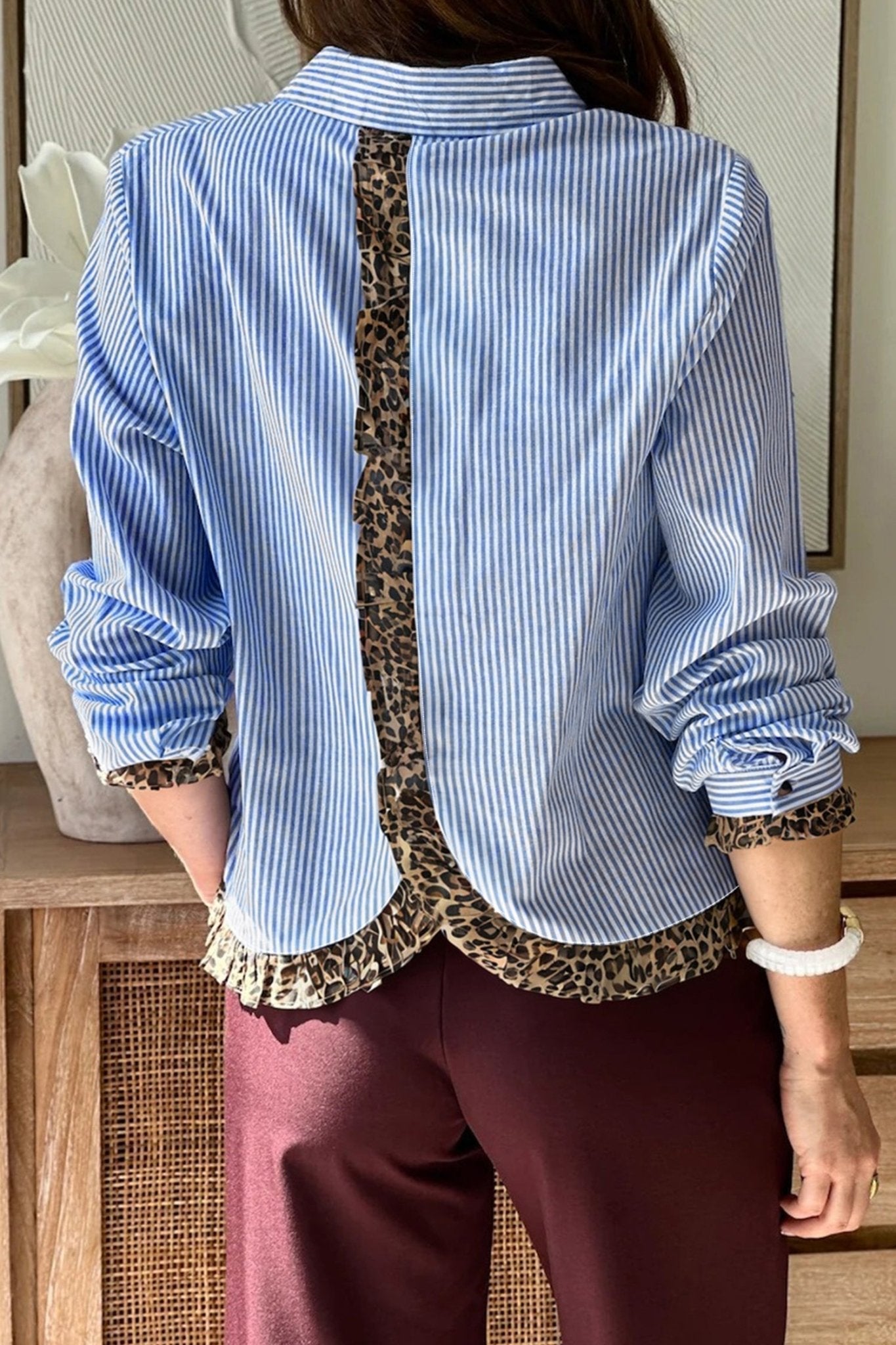 Person wearing a blue striped shirt with leopard print trim and maroon pants.