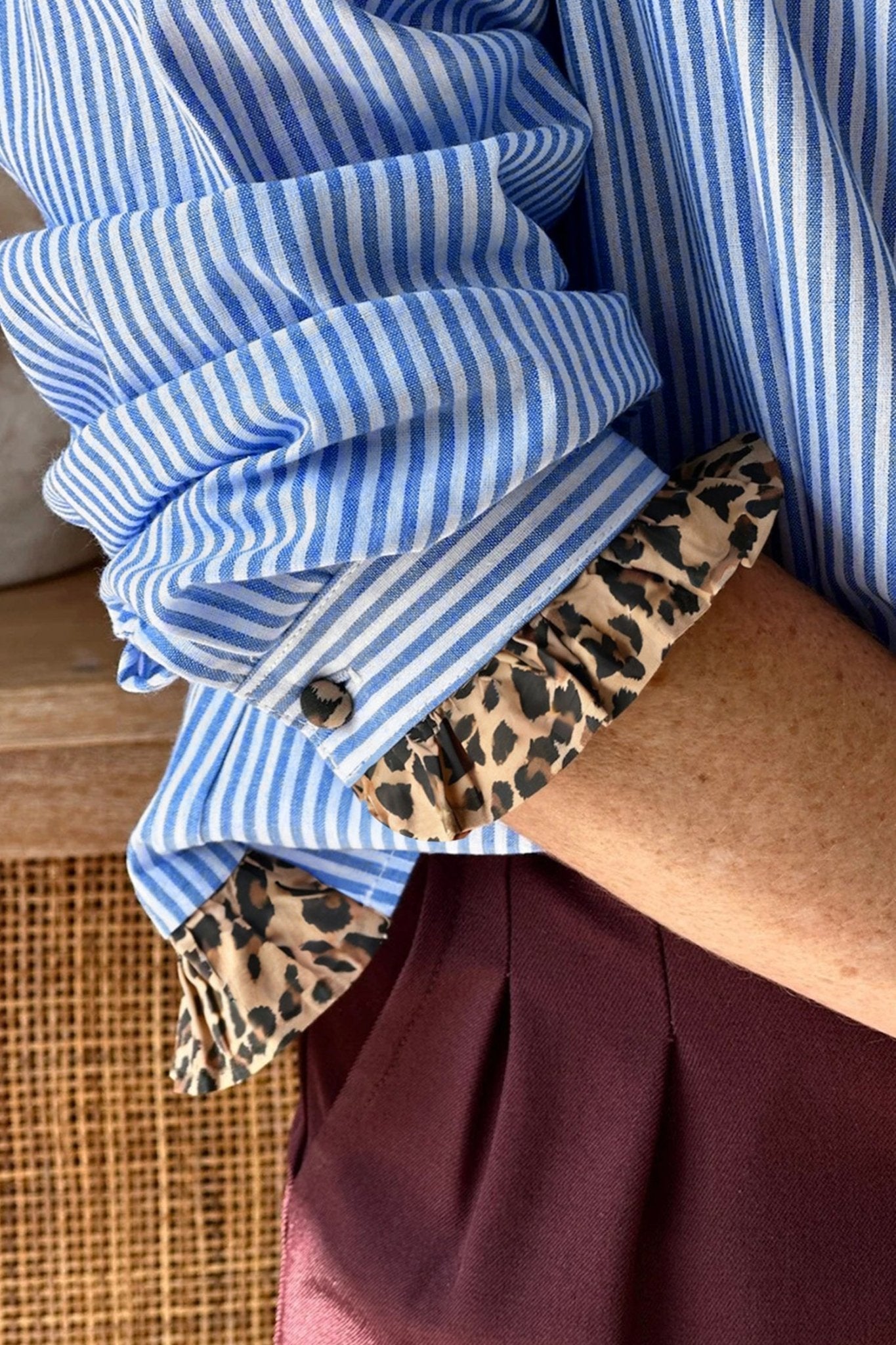 Stack of folded blue and white striped shirts with a leopard print shirt underneath on a wooden surface.