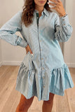 Woman wearing light blue-white striped button-up shirt dress with ruffled details, standing on light wood floors.