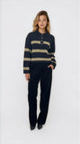 Woman wearing a navy and beige striped sweater with black pants on a white background