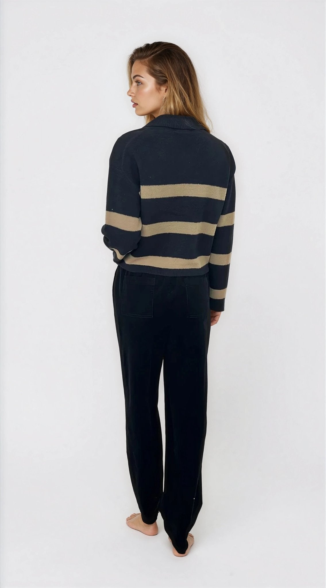 Person wearing a navy sweater with beige stripes and matching pants on a white background