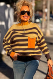 Woman in beige-brown striped sweater with orange pocket, blue jeans, and sunglasses outdoors.
