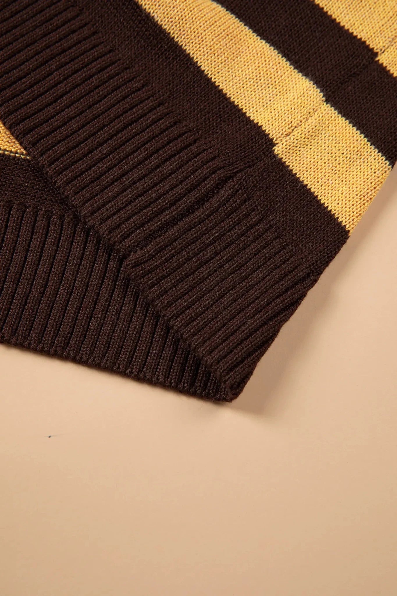 Close-up of ribbed knit fabric with dark brown and mustard yellow stripes on a beige background.
