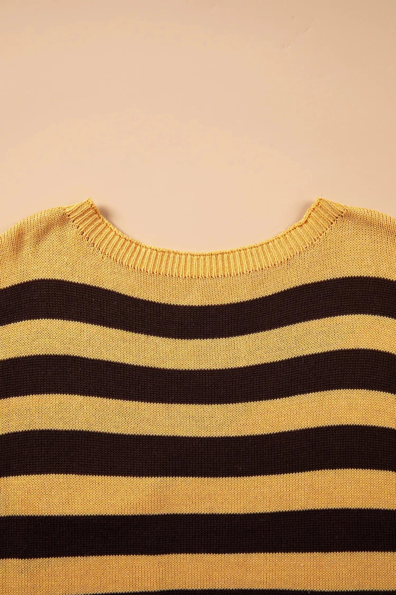 Close-up of mustard and dark brown striped knit sweater with ribbed crew neck on beige.
