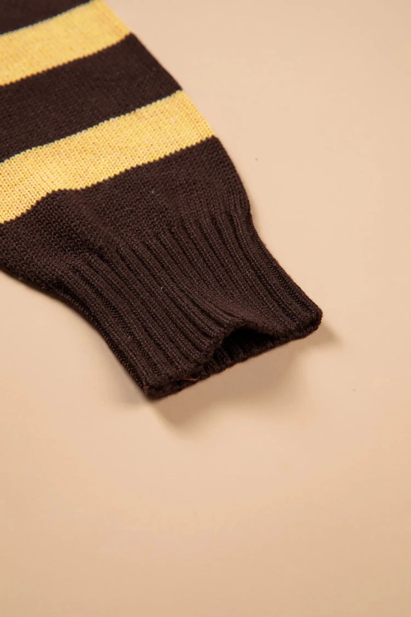 Close-up of dark brown ribbed knit cuff with a mustard yellow stripe on a beige background.
