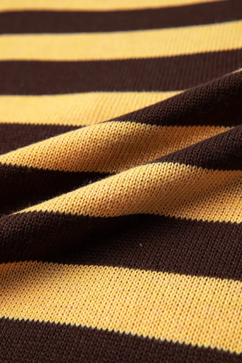Close-up of textured knit fabric with mustard yellow and dark brown stripes and soft folds.
