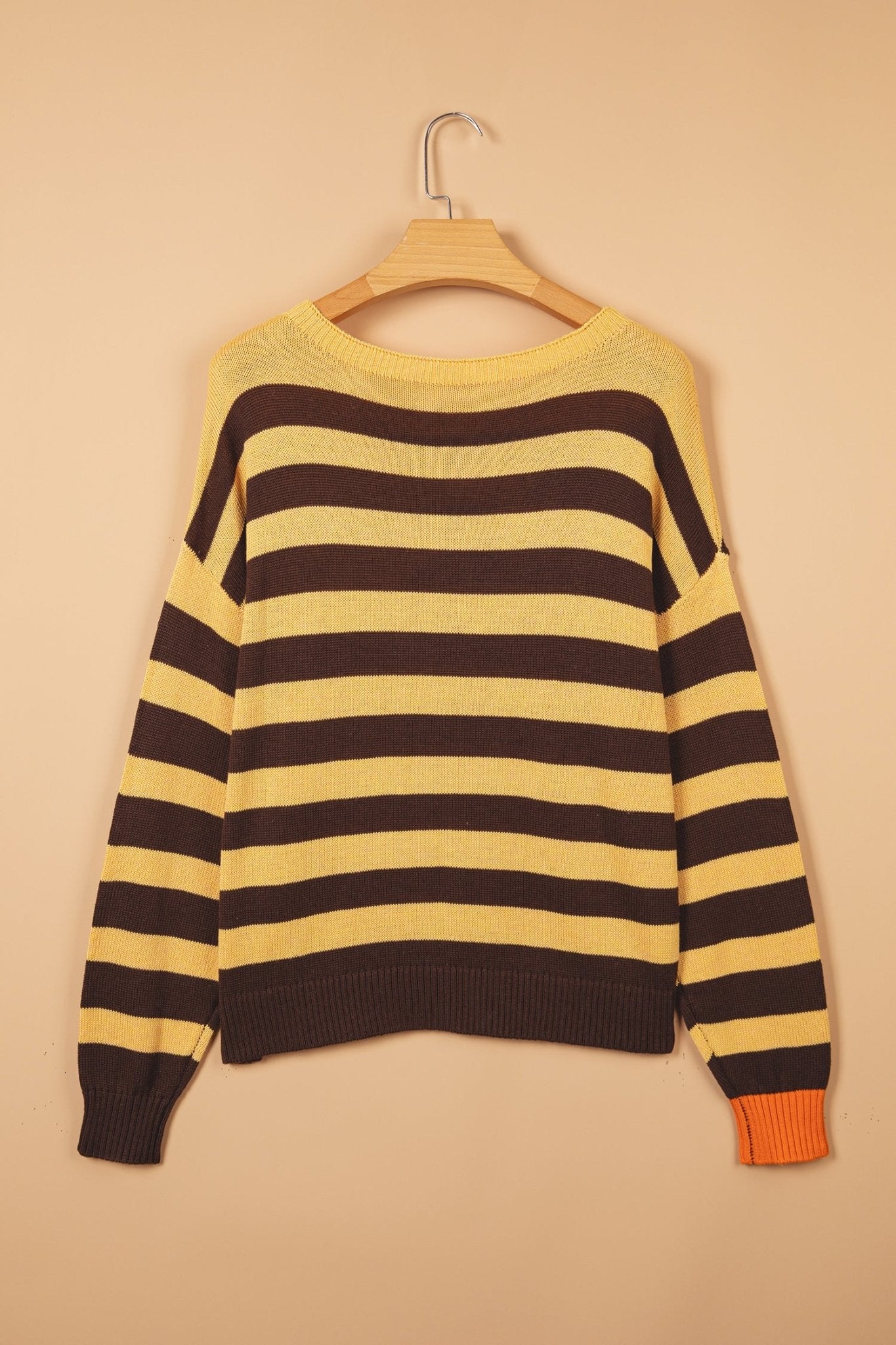 Long-sleeve knit sweater with brown and pale yellow stripes on a wooden hanger against beige.
