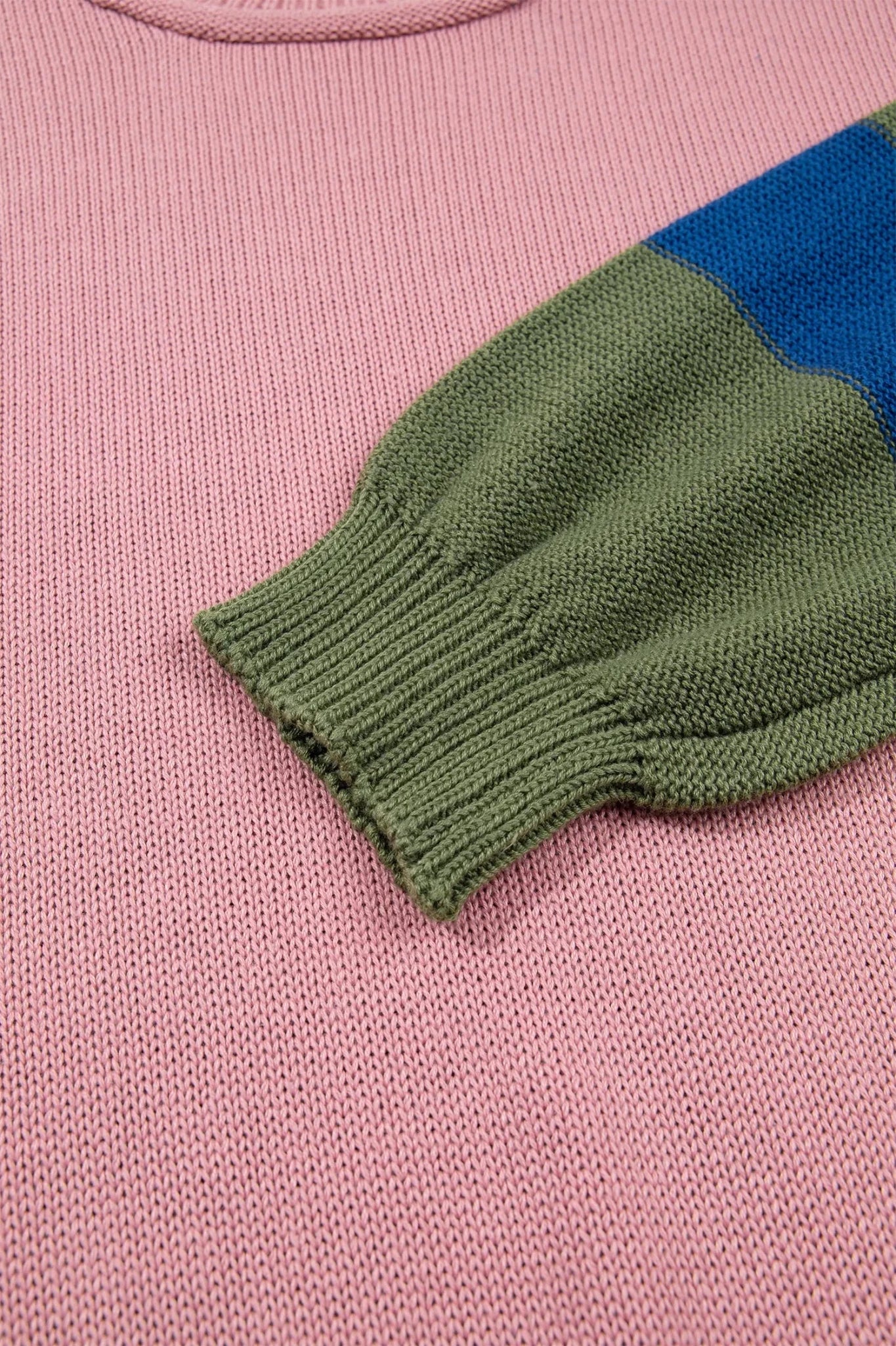 Close-up of a knit sweater showing a ribbed green cuff and a blue color-block section on a pink knit body.