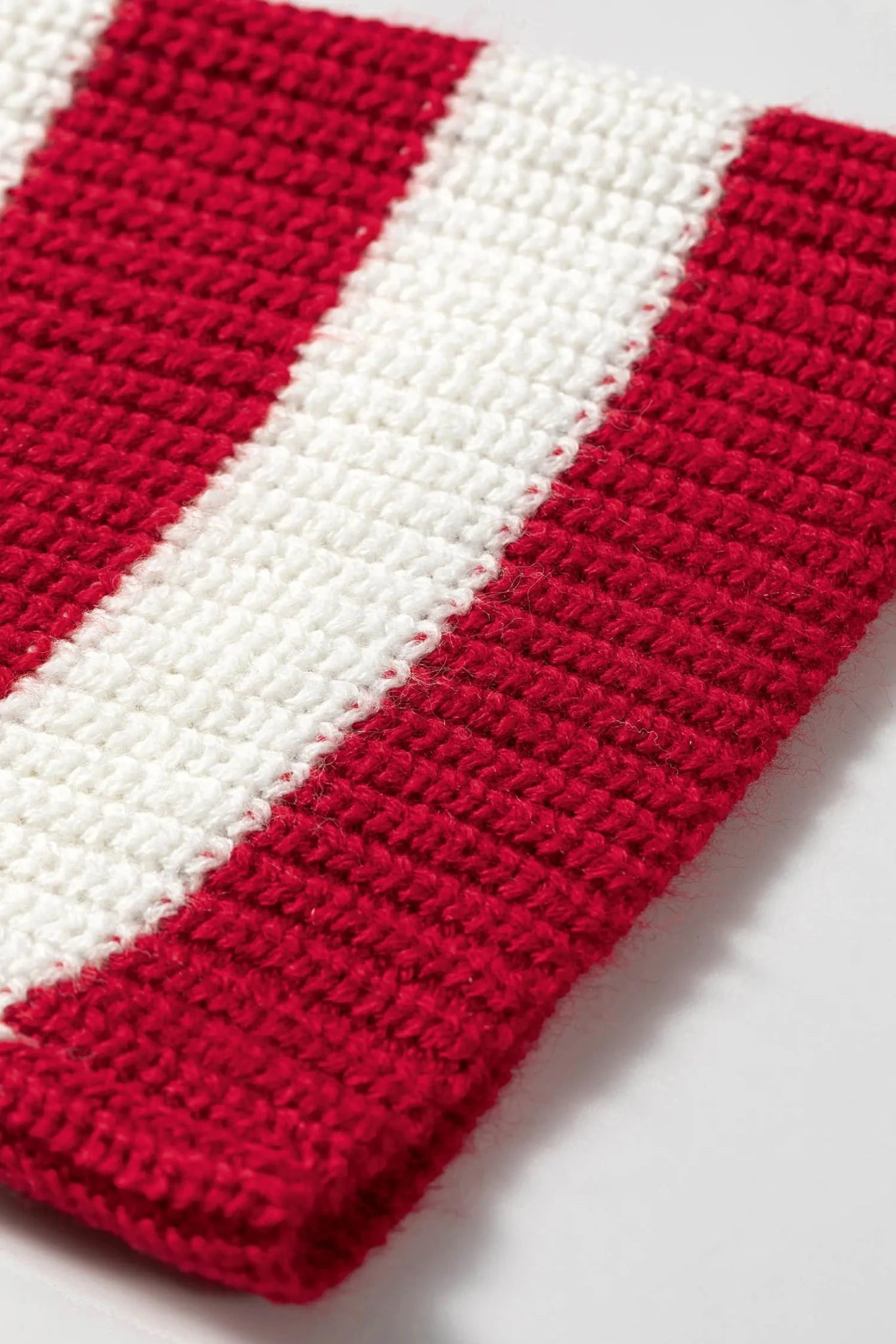 Close-up of bold red and white striped crocheted knit textile on a light neutral background.