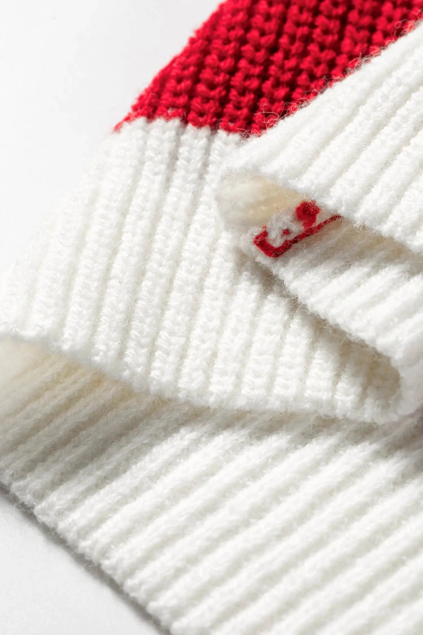 Close-up of white ribbed knit textile with red knit section and embroidered logo on cuff.