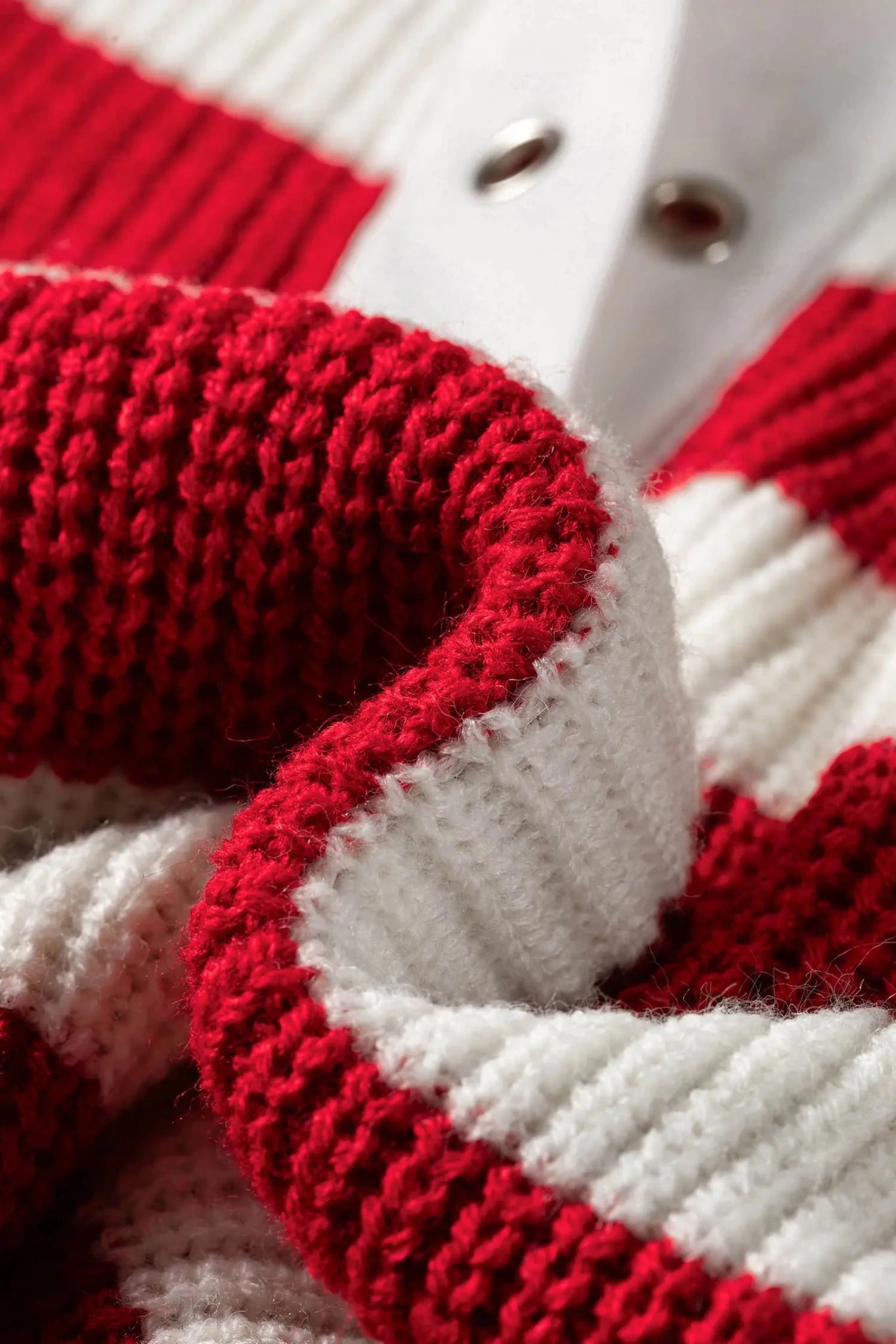 Close-up of red and white striped knit garment with ribbed trim and metal snap buttons.