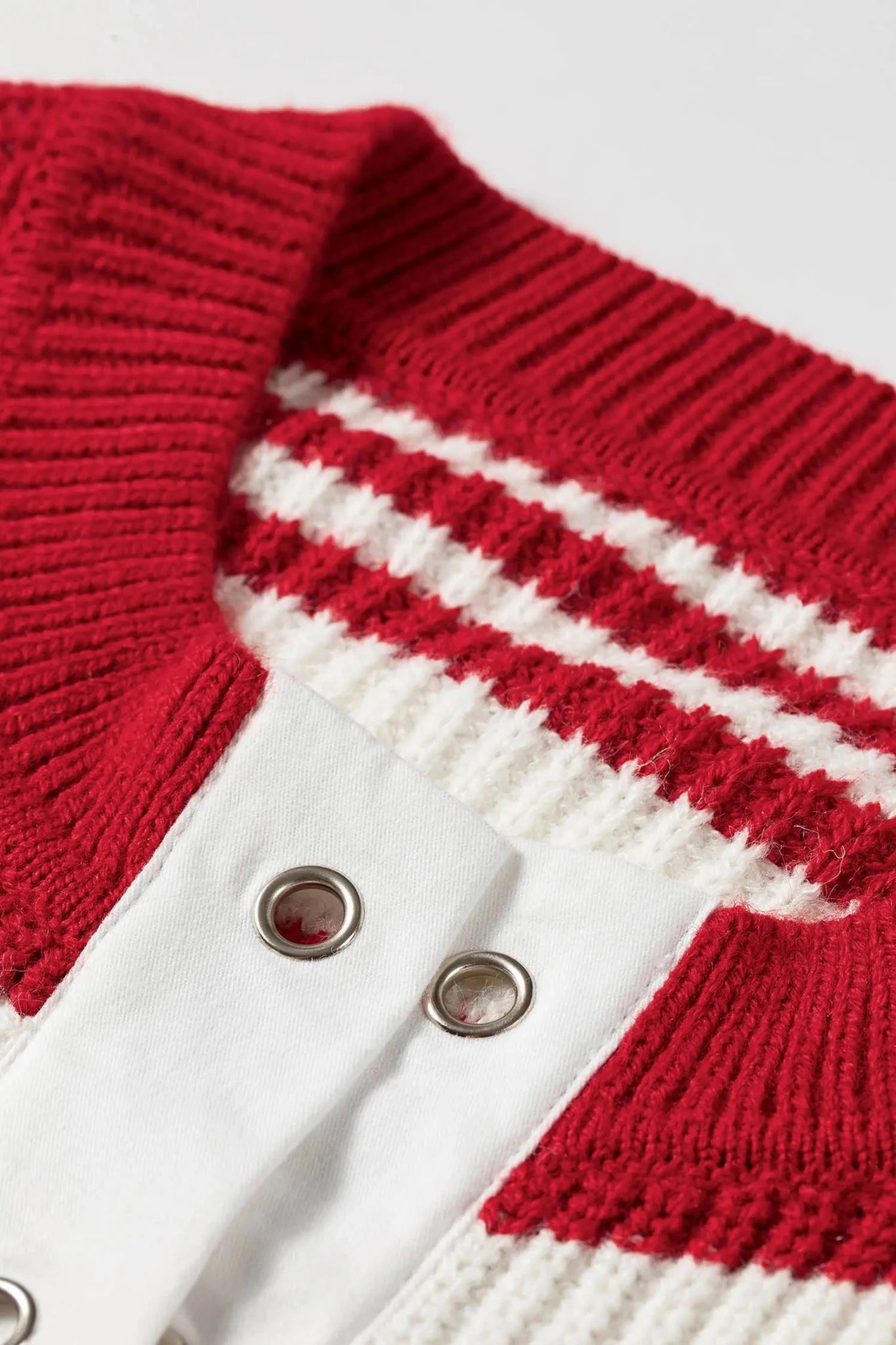 Close-up of red and white striped knit cardigan with white panel and metal snap buttons.