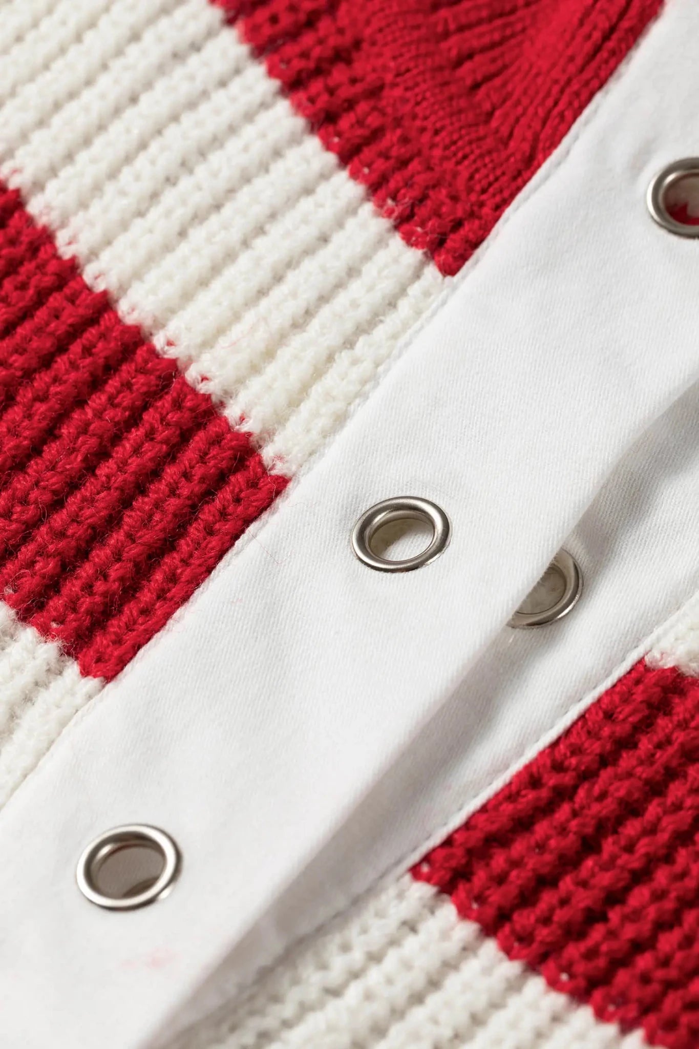 Close-up of red and off-white striped knit cardigan with white button placket and silver grommets.