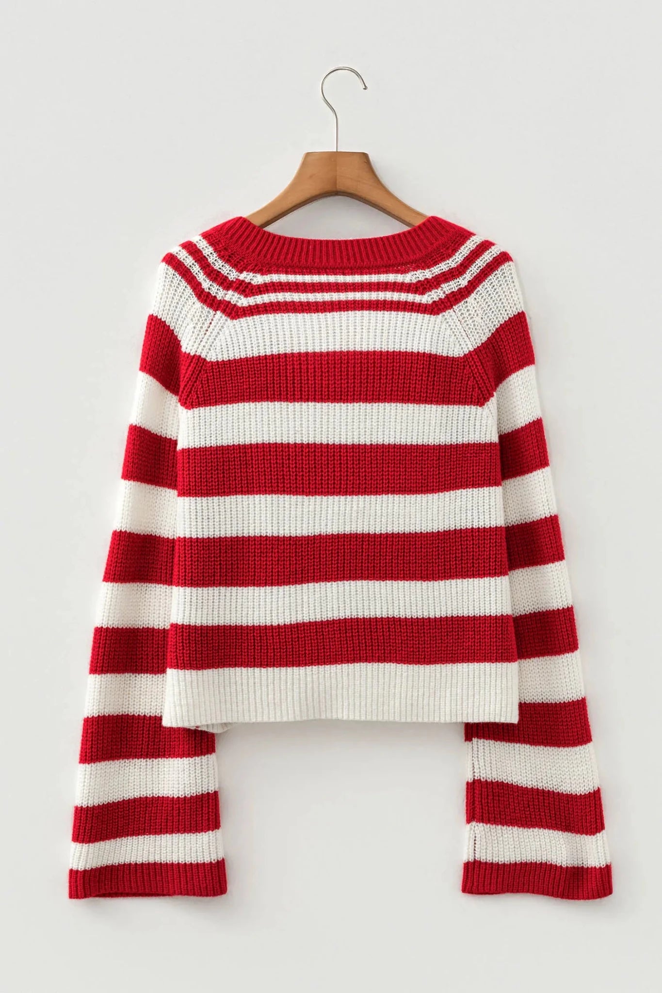 Red and white striped knit sweater with long sleeves hanging on a wooden hanger, gray background.