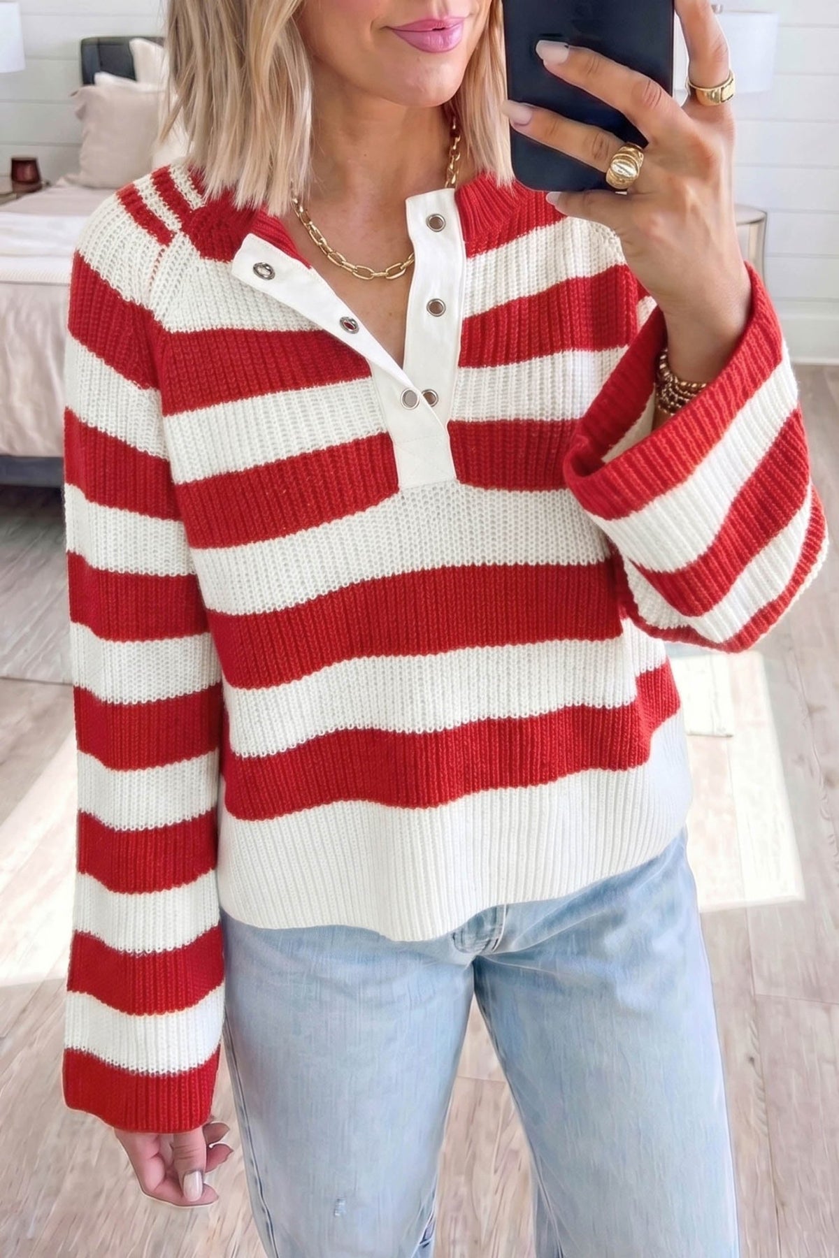 Woman taking mirror selfie in red and off-white striped henley knit sweater with light blue jeans.