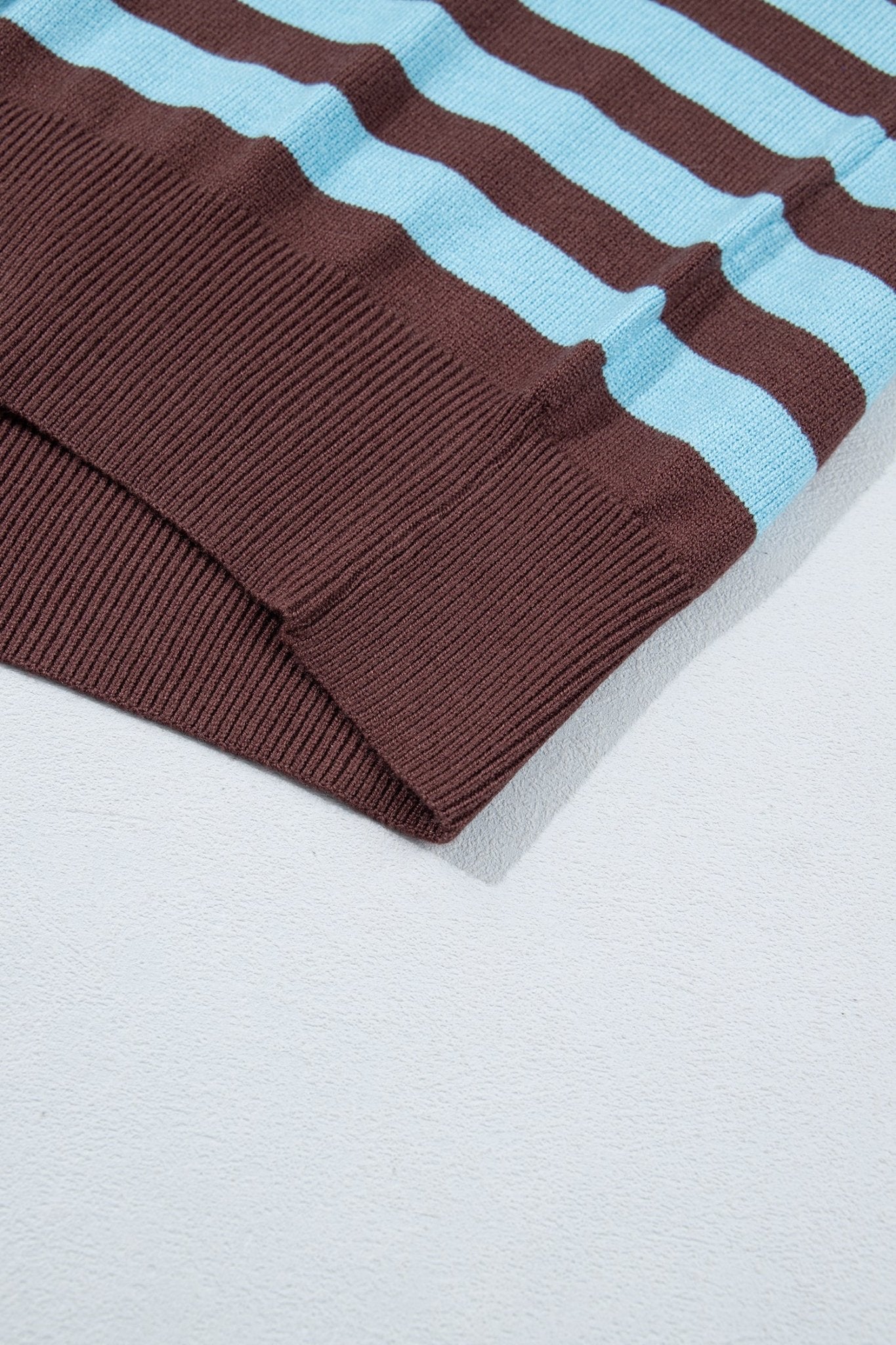 Close-up of ribbed knit garment with alternating brown and light blue stripes on a white textured background.