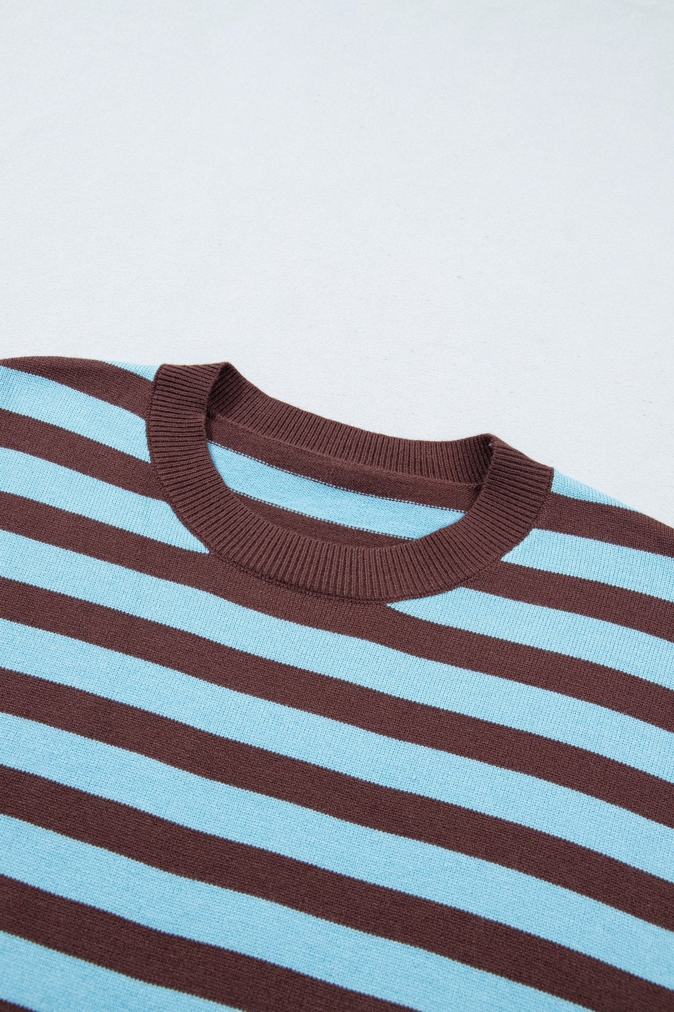Close-up of striped knit sweater with ribbed brown crew neck and alternating light blue and dark brown stripes.