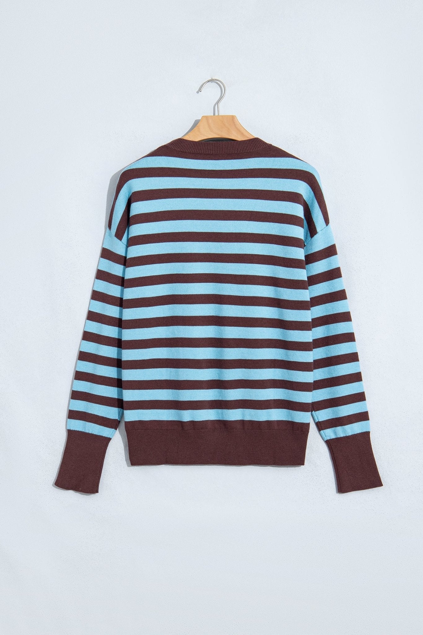 Striped knit sweater with light blue and dark brown horizontal stripes, hanging on a wooden hanger.