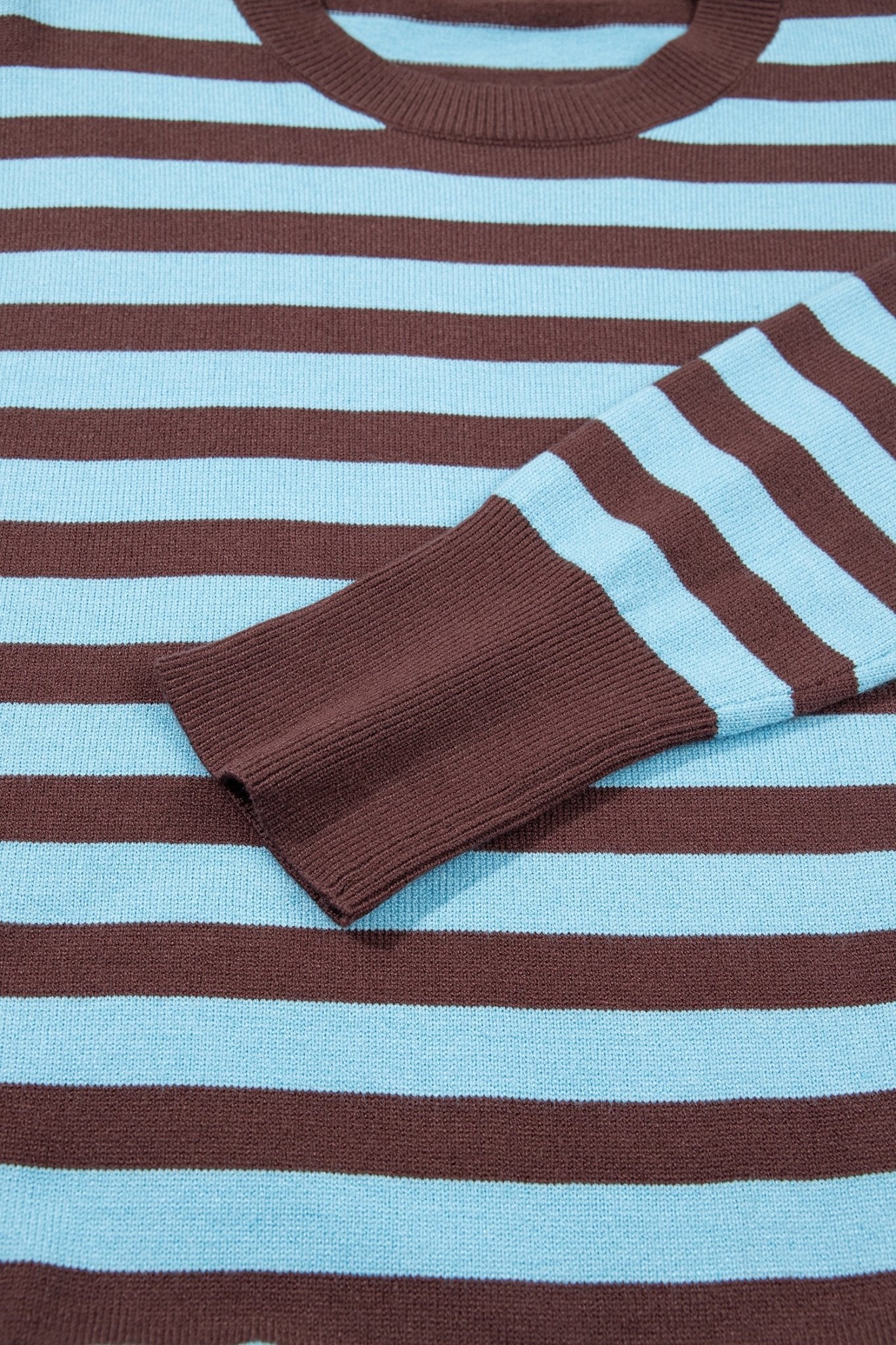Close-up of a ribbed knit sweater with horizontal brown and light blue stripes, showing the crew neck and folded sleeve cuff.