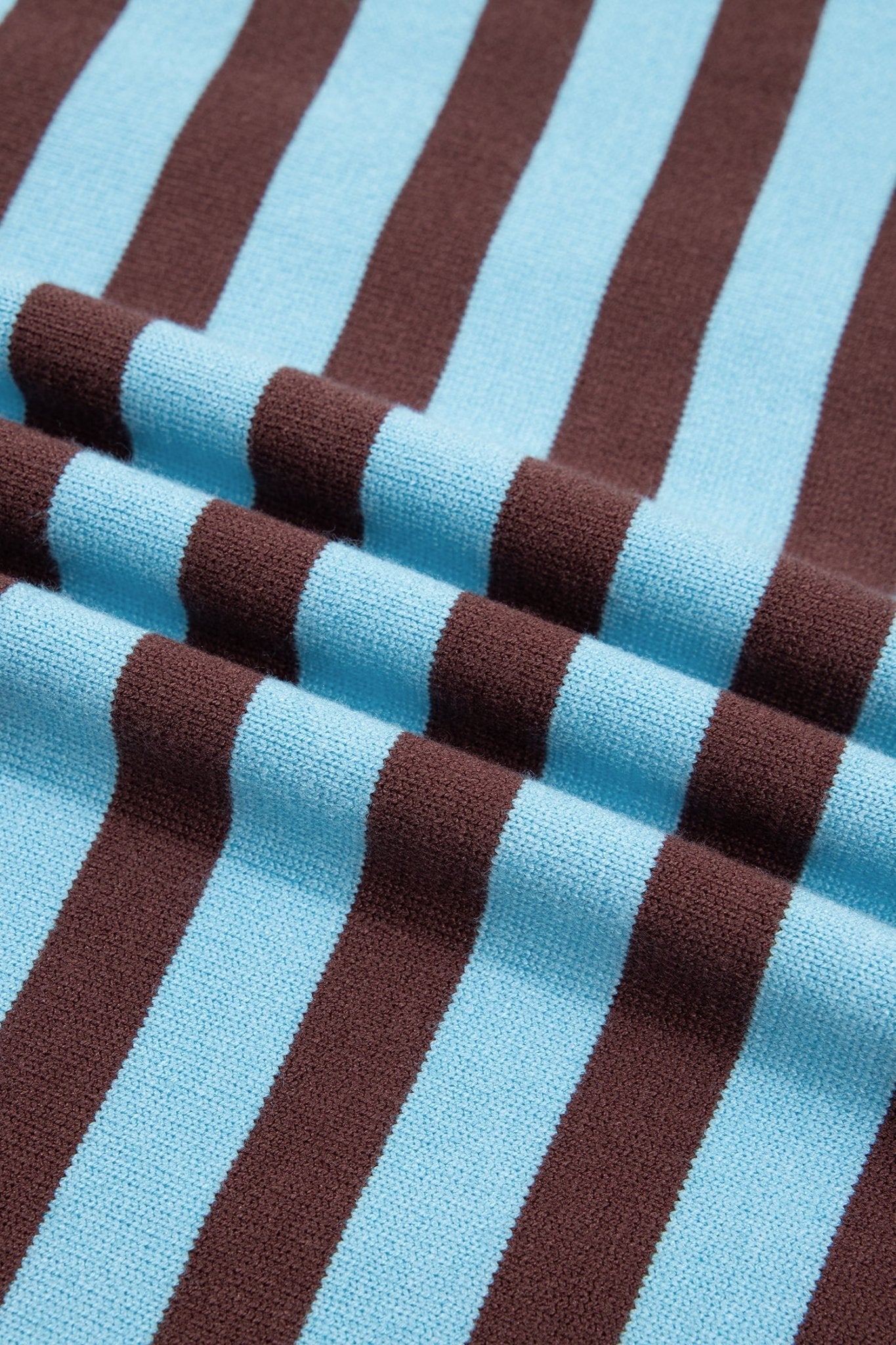A close-up of a striped knit fabric with alternating light blue and dark brown vertical stripes, shown with soft folds.