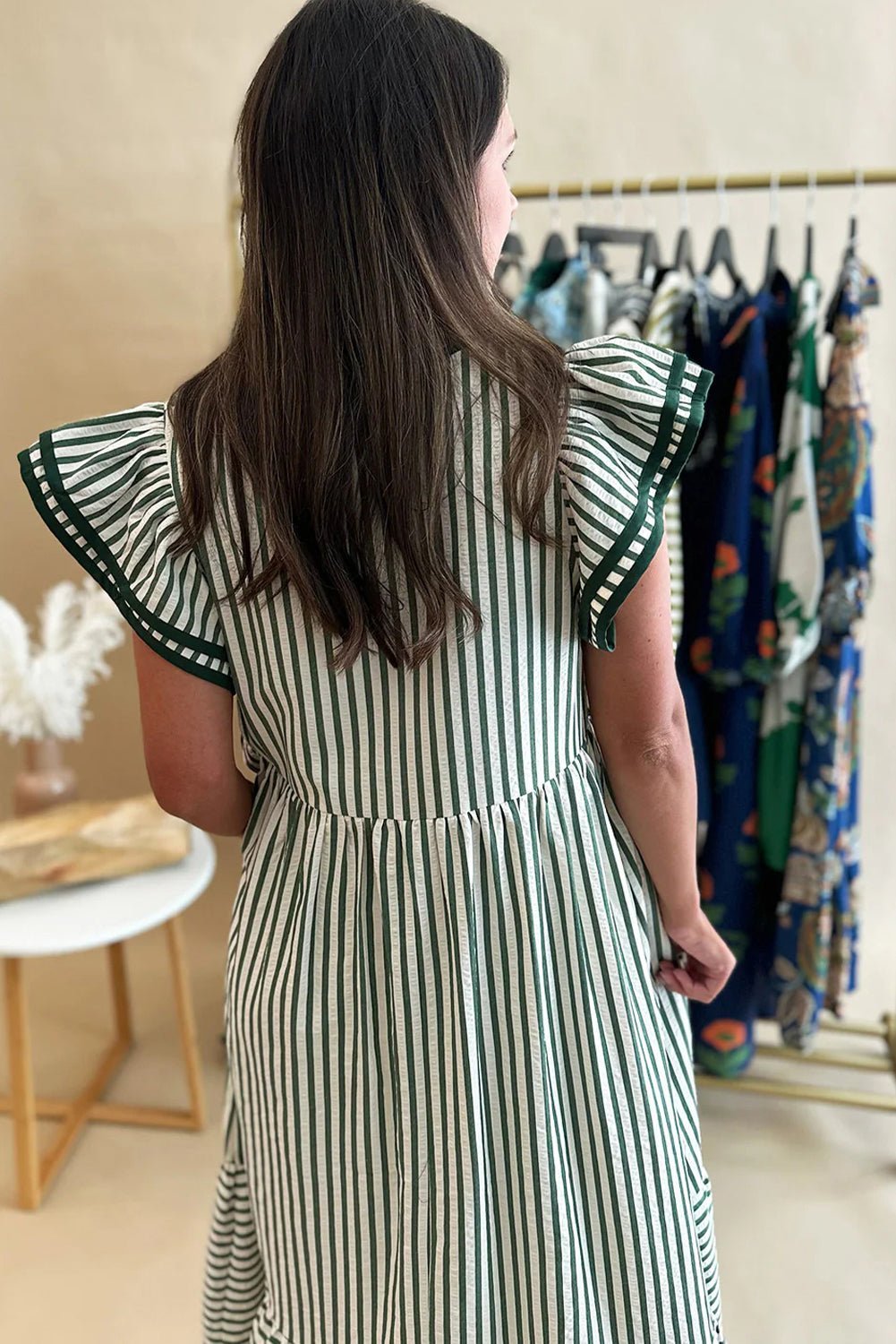 Woman wearing a green and white striped dress with ruffled sleeves in a clothing store.