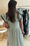 Woman wearing a green and white striped dress with ruffled sleeves in a clothing store.