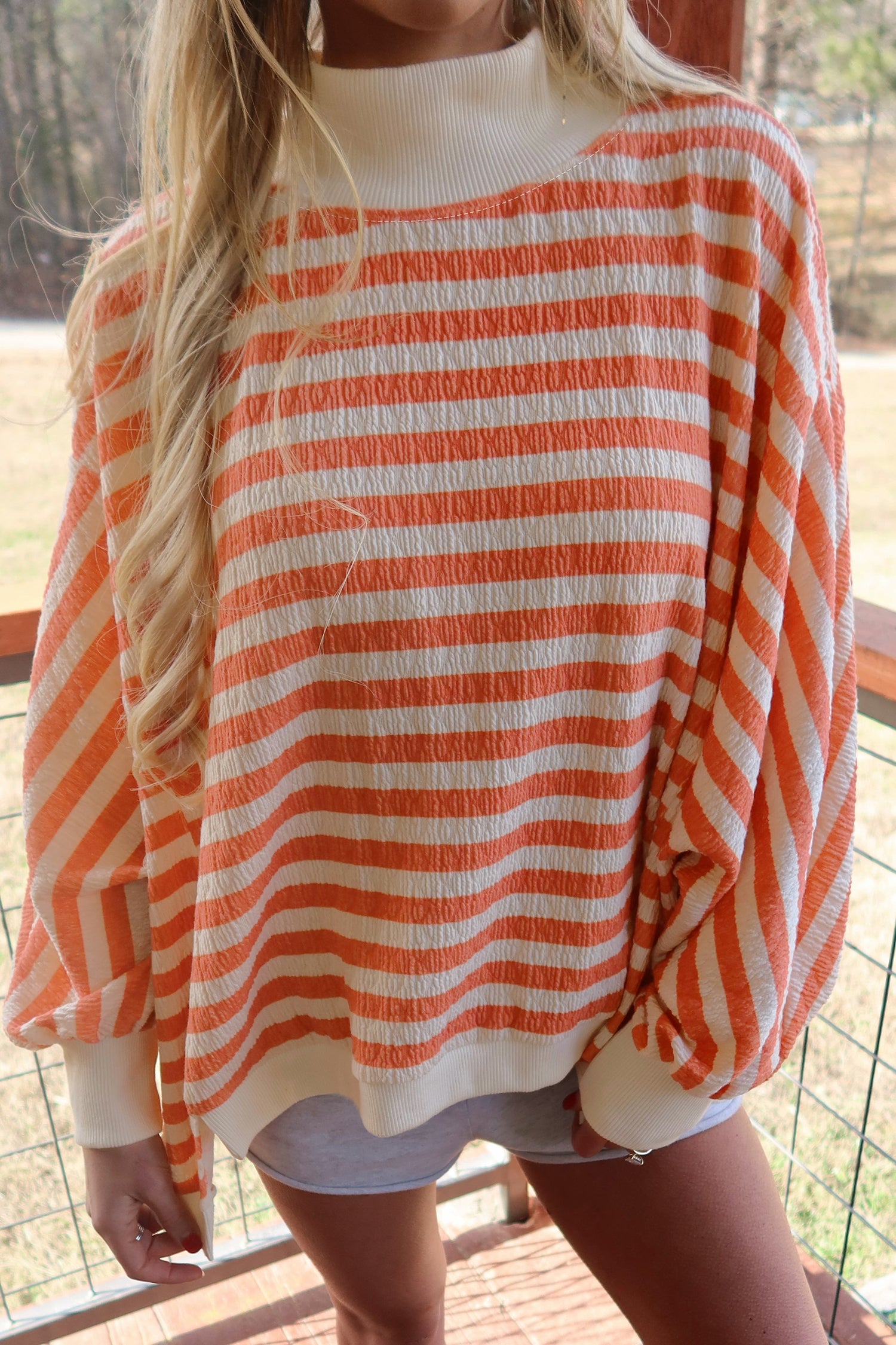 Oversized orange striped mock neck top with ribbed cream cuffs, close front view