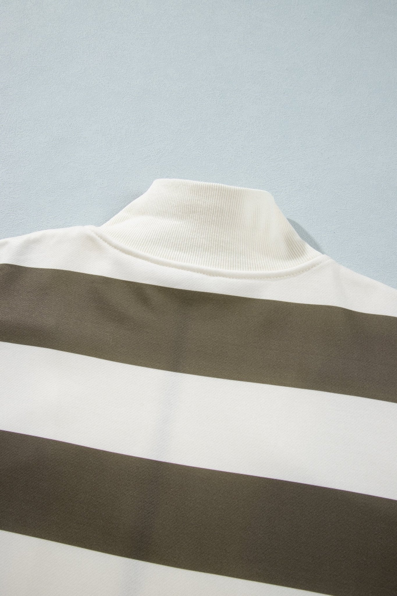 Close-up of off-white and dark olive green striped knit top with ribbed mock neck on light blue-gray.