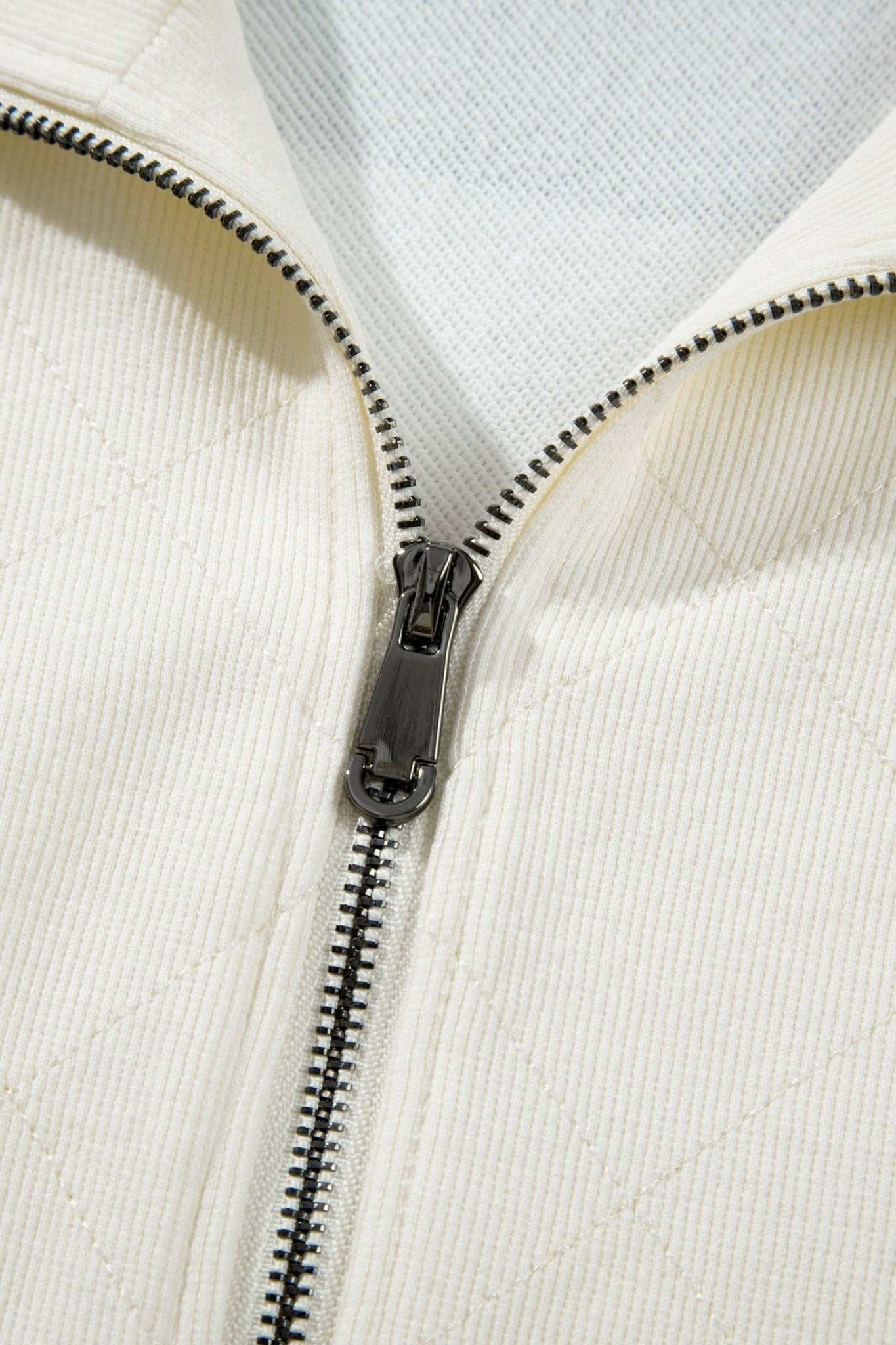 Close-up of a cream-colored zippered jacket with a black metal zipper and a light gray ribbed inner collar.