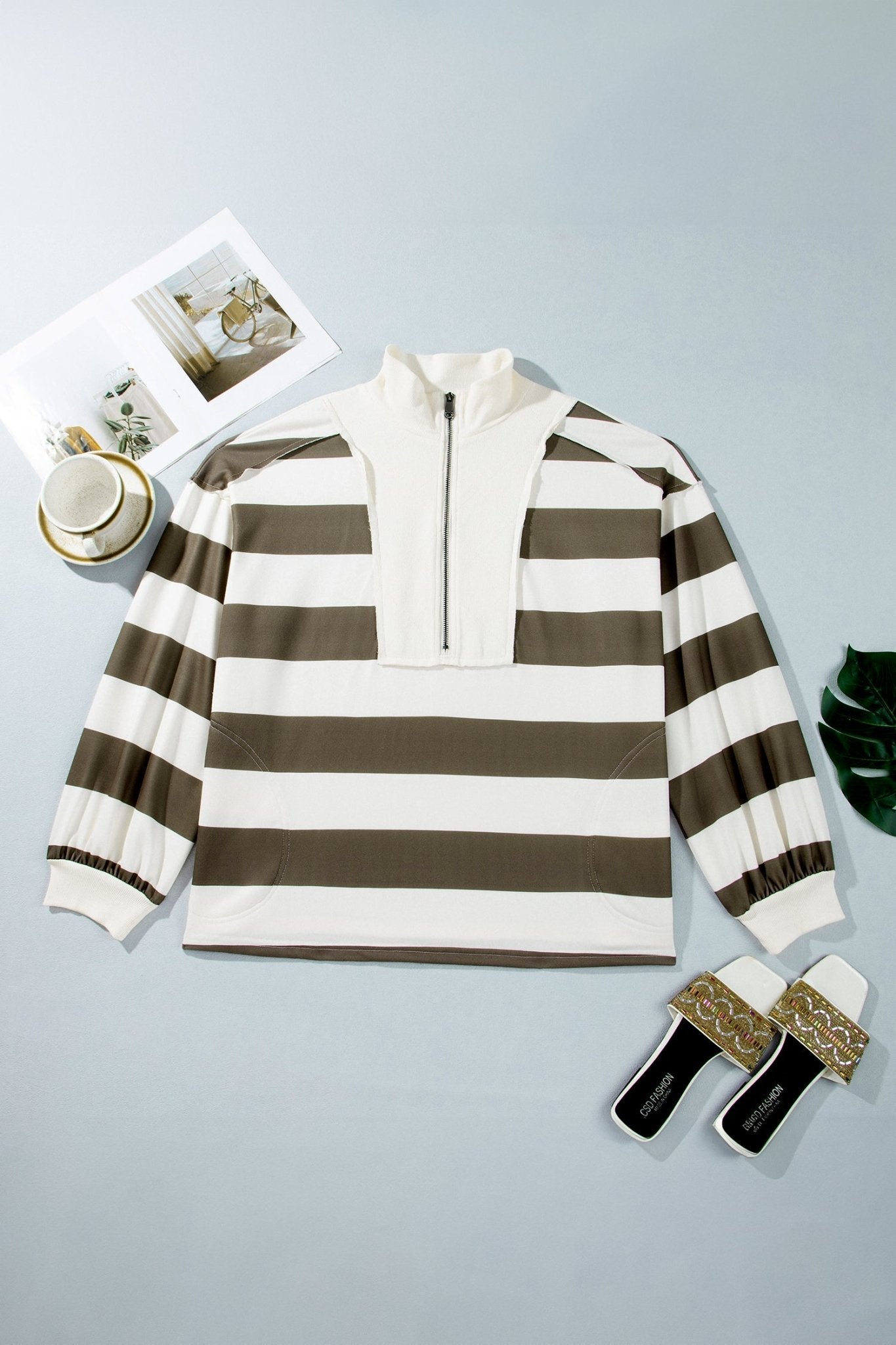 Olive brown and off-white striped quarter-zip flat lay with cup, magazine, and shoes on light blue-gray.