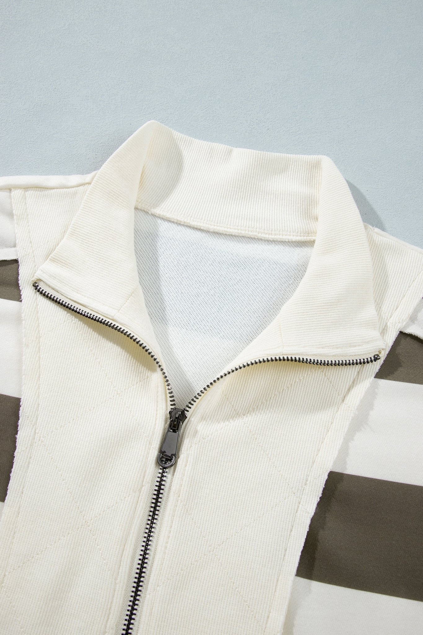 Close-up of cream zip-up vest with dark brown side stripes on light gray.