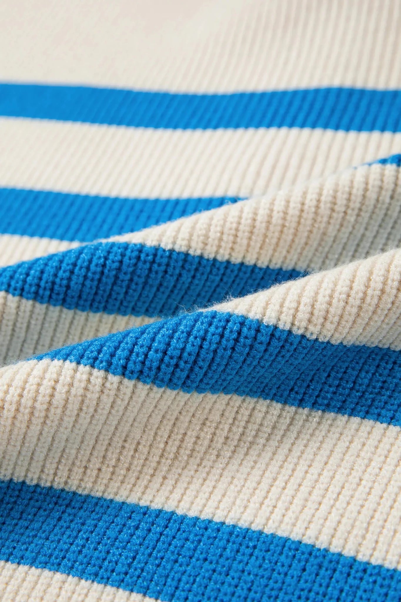 Close-up of a ribbed knit fabric with horizontal stripes in bright blue and warm off-white/cream.