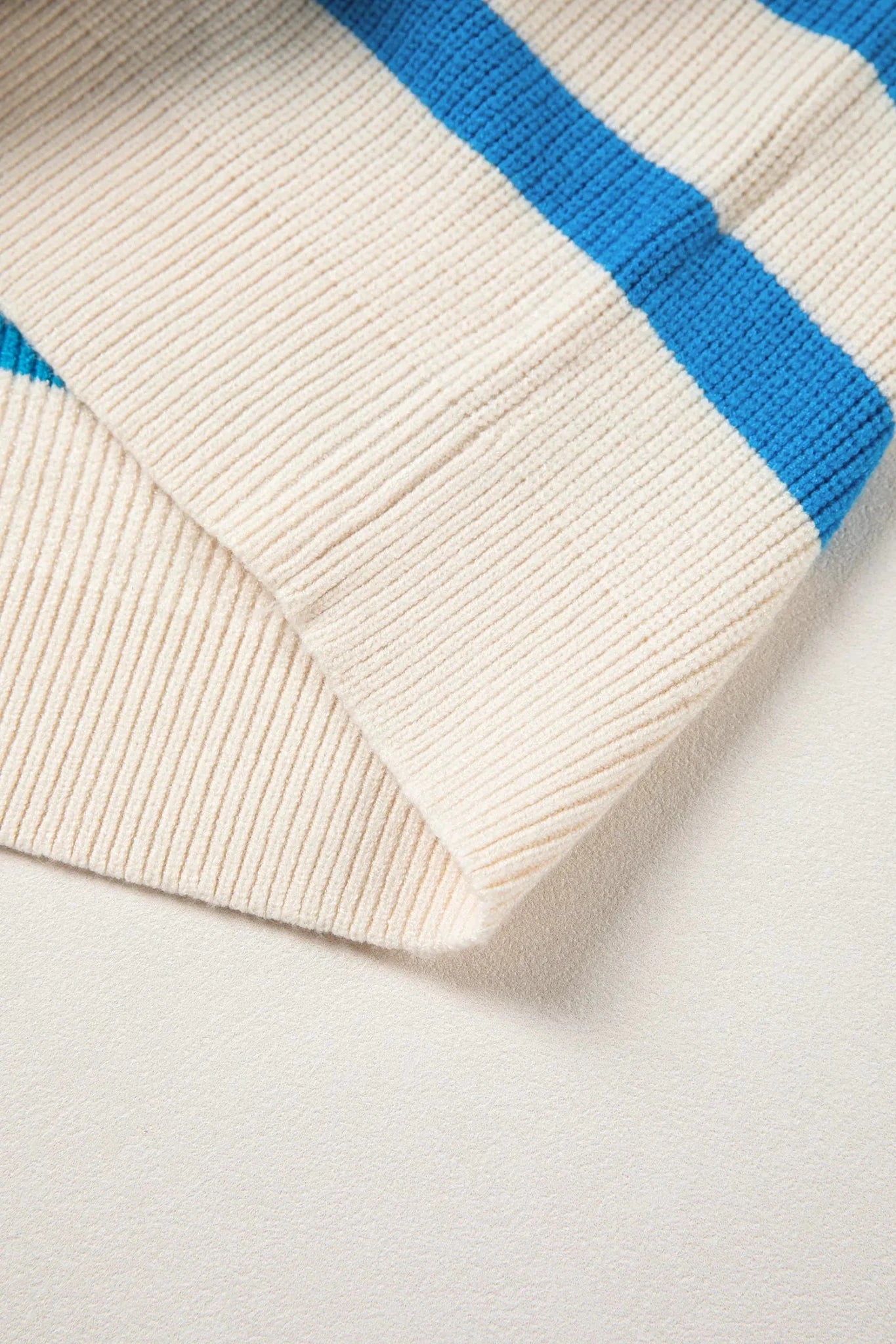Close-up of a cream-colored sweater with blue stripes on a light gray background