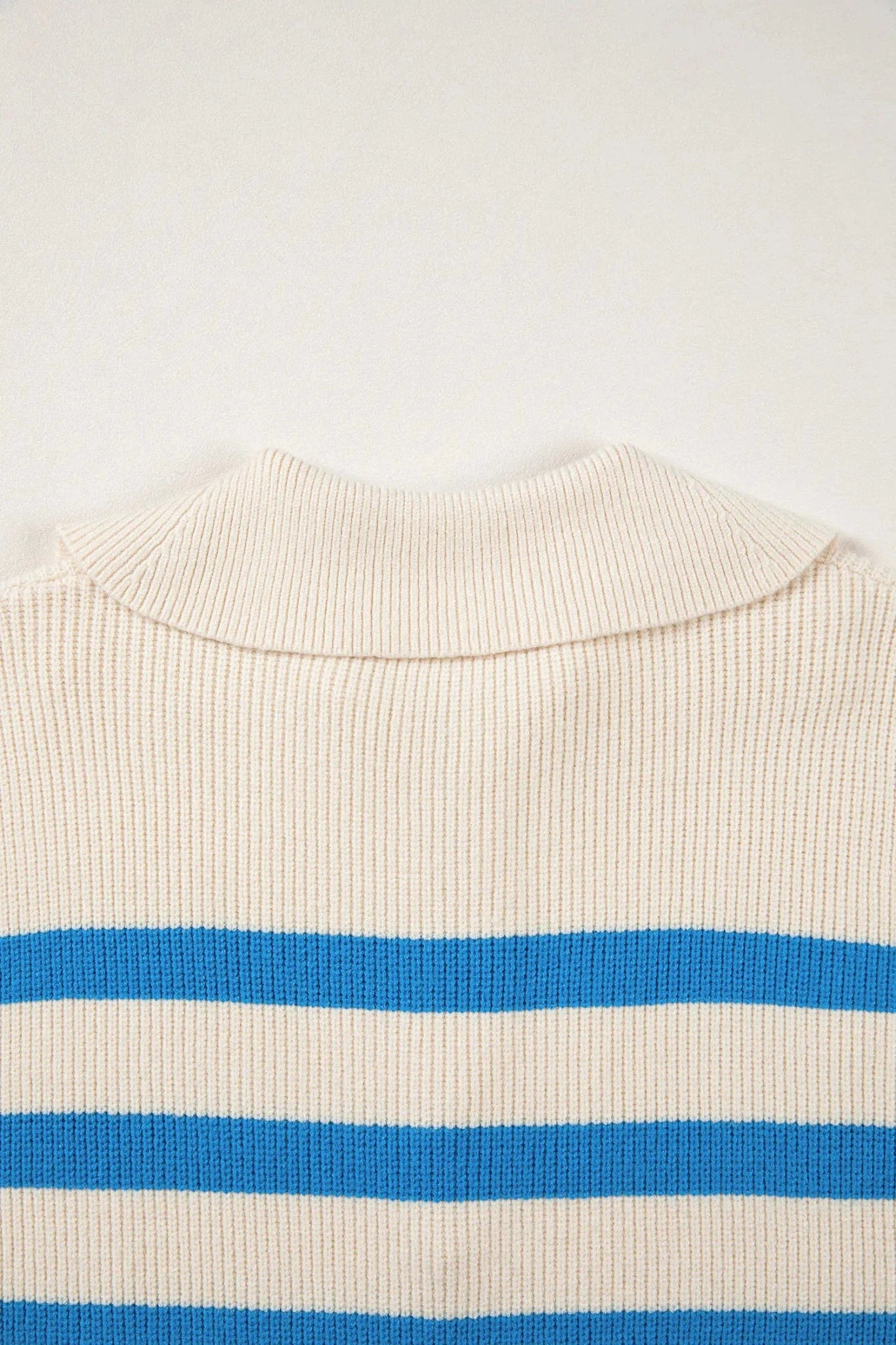 Close-up of a ribbed knit sweater with a cream base and bold blue horizontal stripes, showing the collar area against a plain light background.